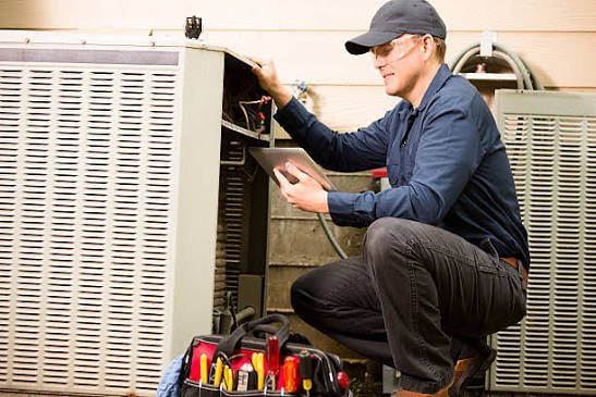 HVAC technician inspecting an outdoor heating and cooling unit beside a home